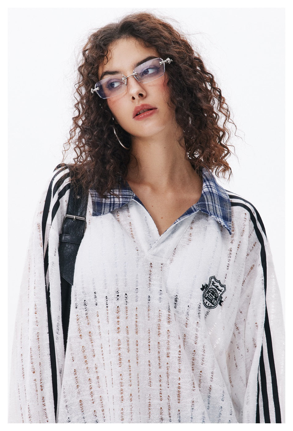 Close view of a model wearing a white open-knit polo with black sleeve stripes, a blue plaid collar and chest crest.