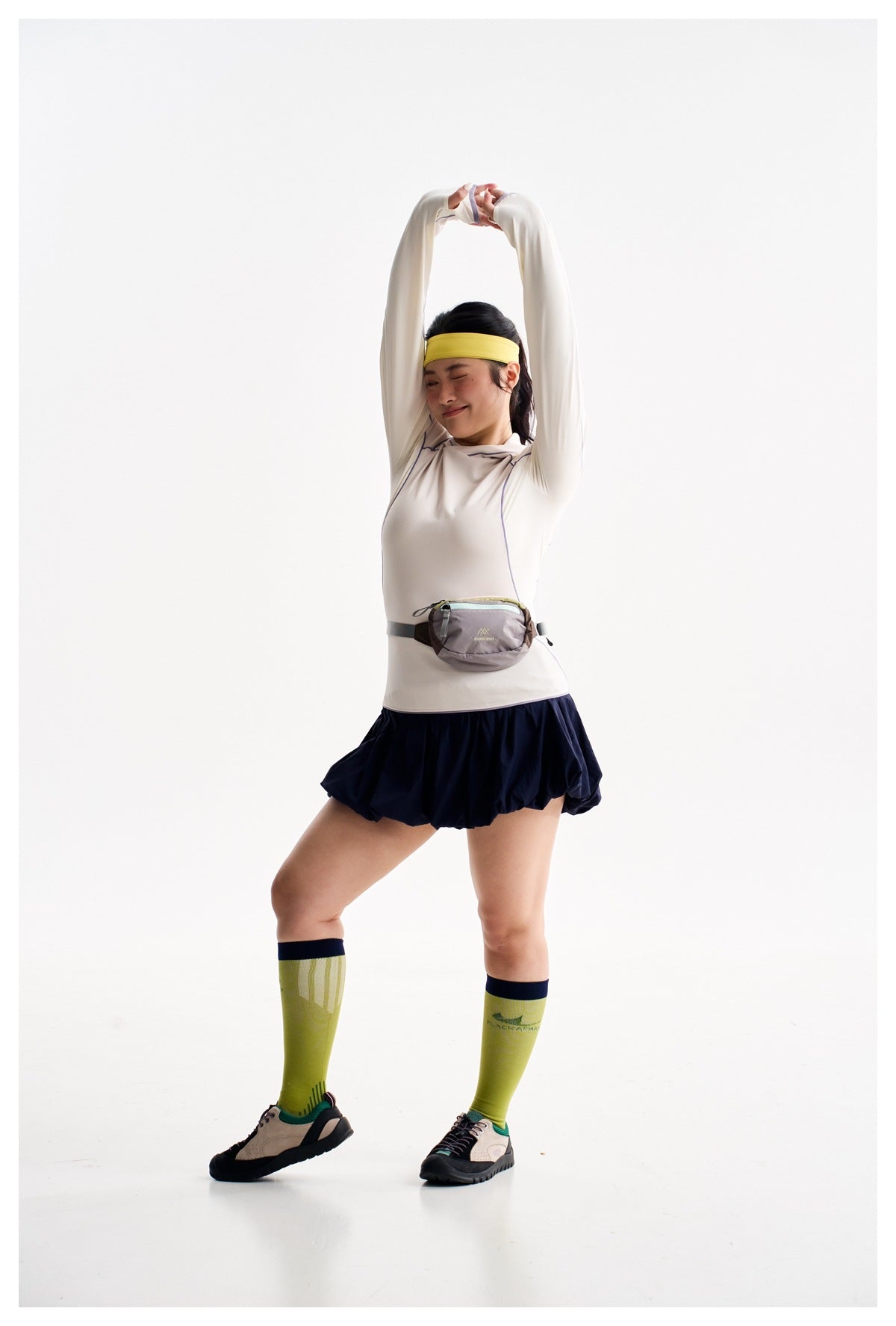 Model stretching in an ivory long-sleeve top with purple piping and a navy bubble-hem skirt.