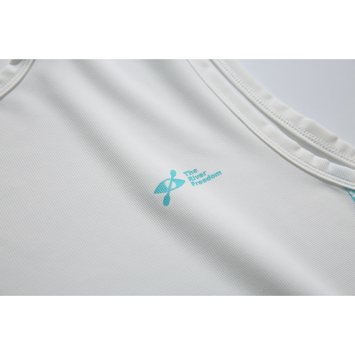 Close-up of a white textured top showing its turquoise chest emblem and bound neckline and armhole.