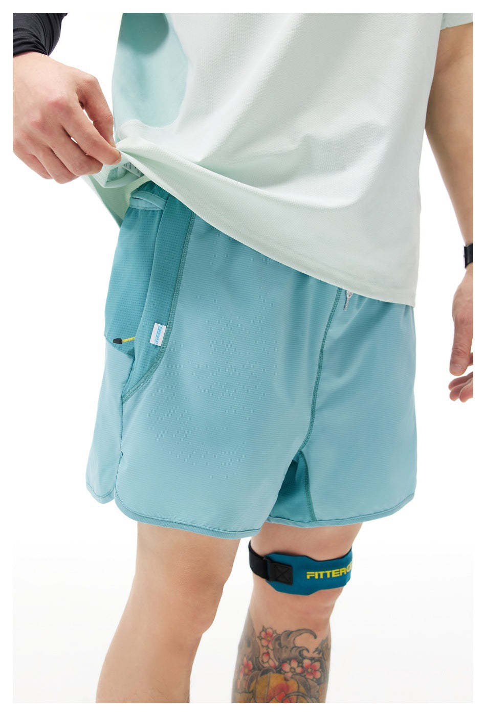 Close-up of a person wearing light teal-blue shorts with a side pocket, tucked-up light top and a leg strap