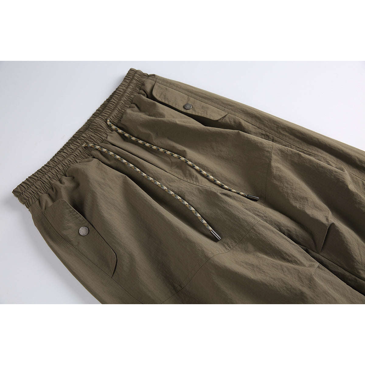 Close-up of olive-brown cargo pants showing the elastic waistband, braided drawcord, and flap pockets.