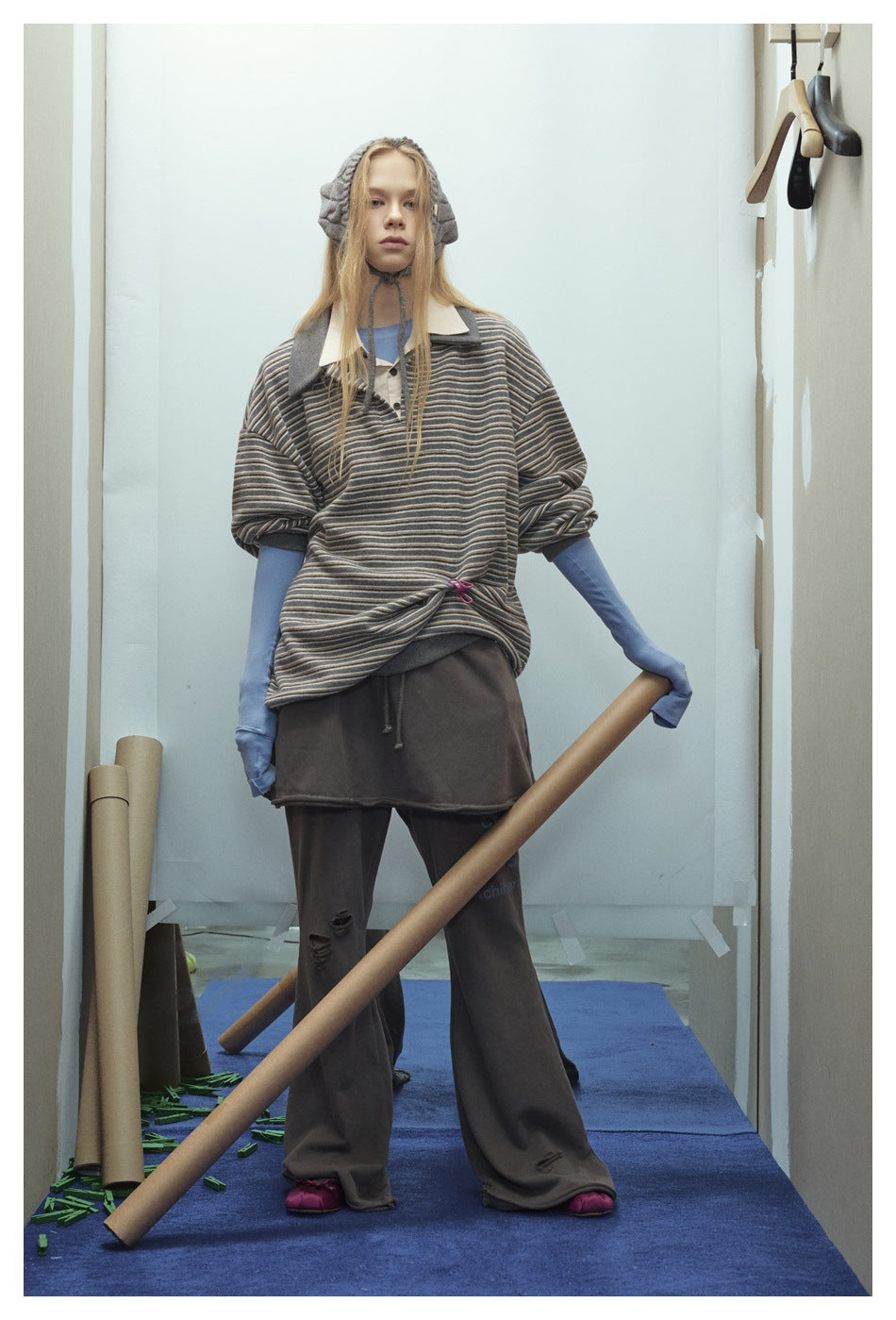 Full-length model in a loose gray striped polo over blue sleeves and distressed dark wide-leg pants.