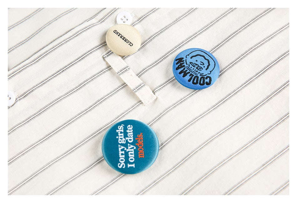Close-up of white fabric with fine dark diagonal stripes, a white button, and blue slogan patches.