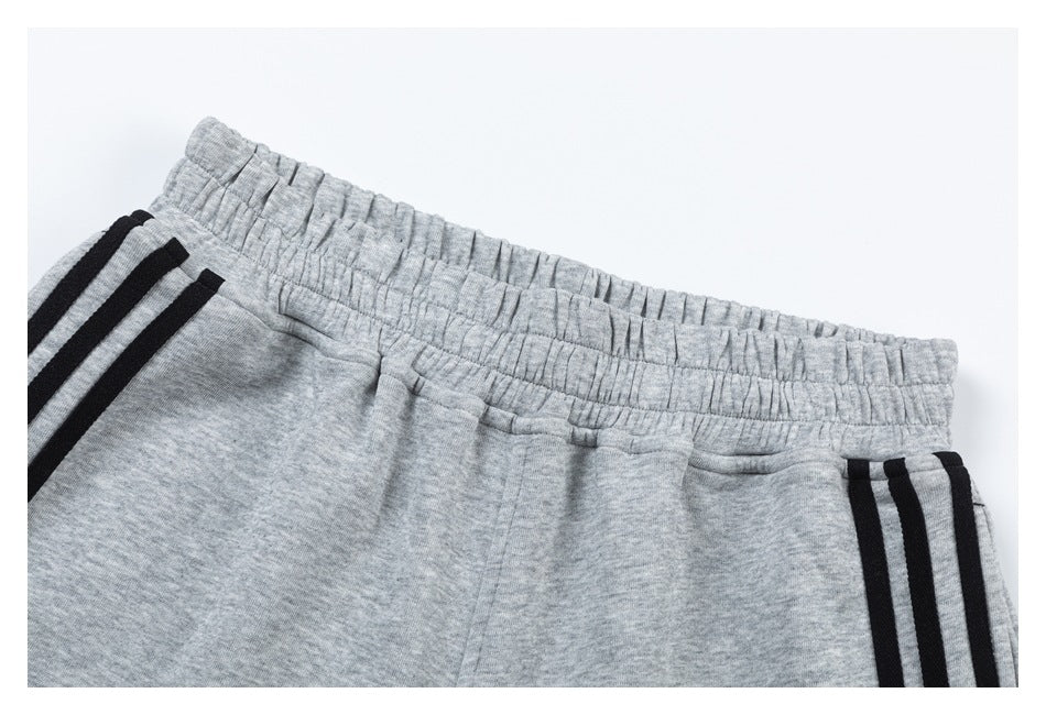 Close-up of light gray pants showing the gathered elastic waistband, pocket edge, and black side stripes.