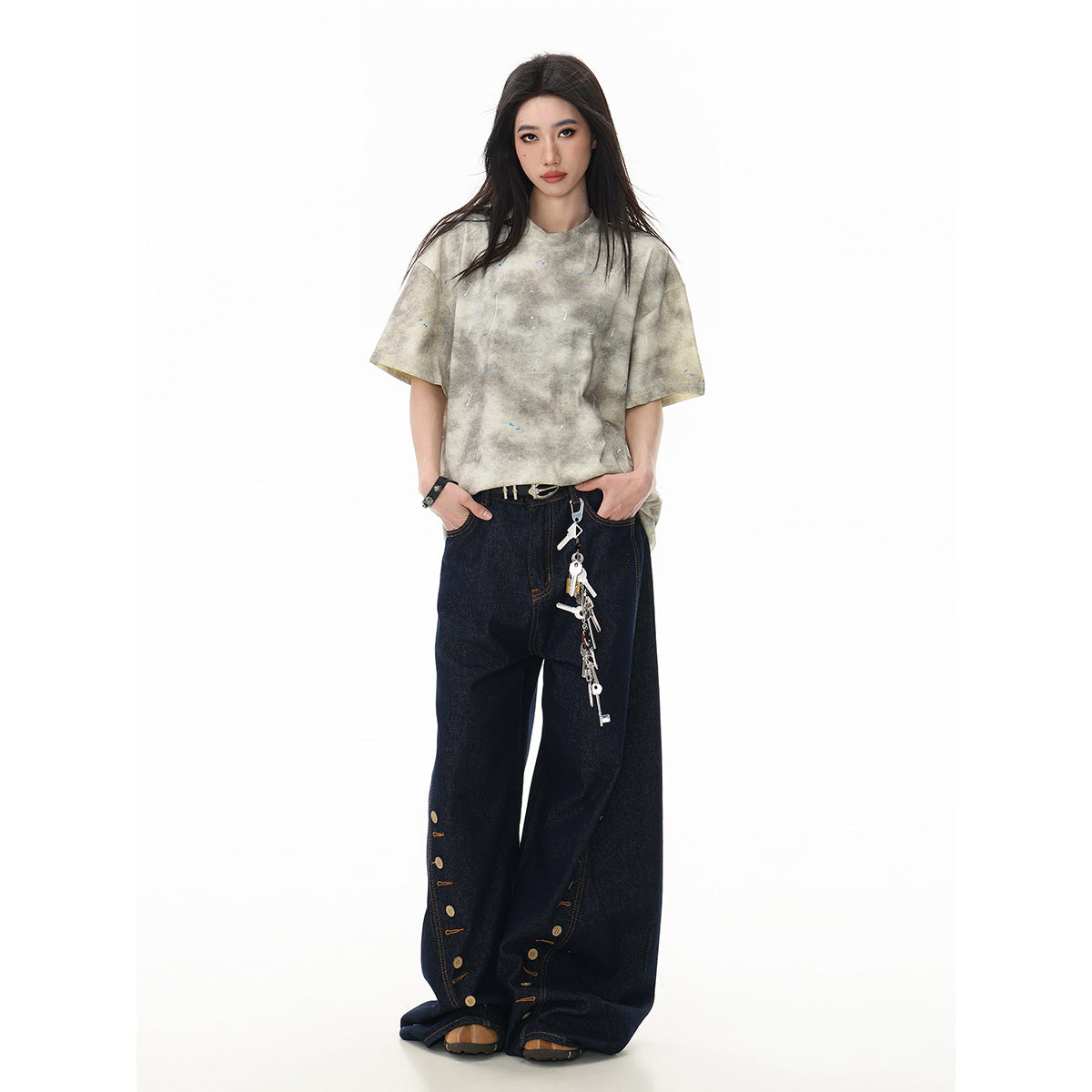 Full-length front view of a model in a beige-gray mottled oversized T-shirt and wide dark jeans with button details.