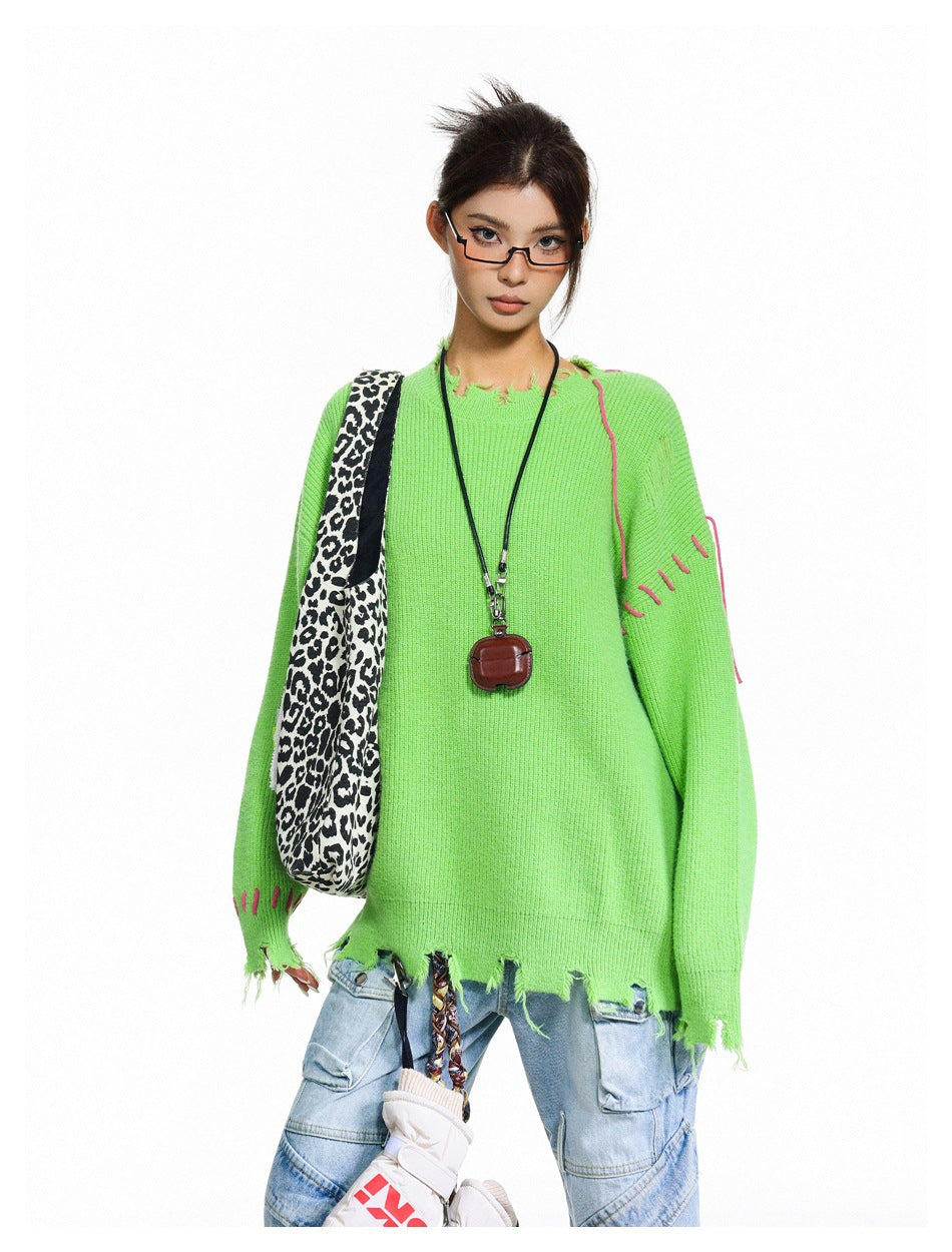 Close view of a model wearing a neon-green oversized sweater with pink stitch accents and a distressed hem.