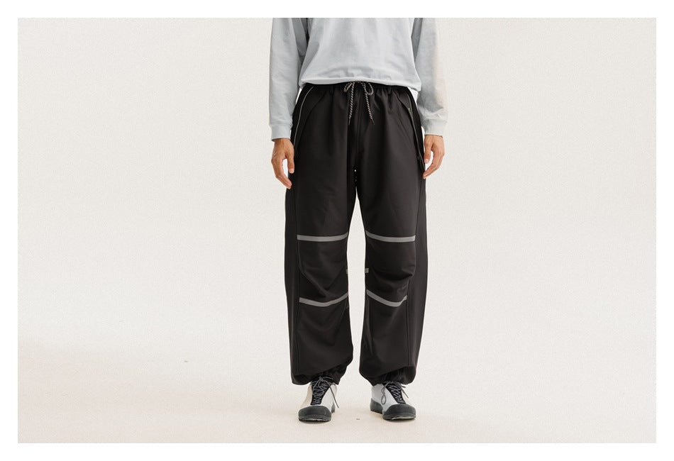 Front view of a model wearing loose black drawstring pants with gray bands across the legs.