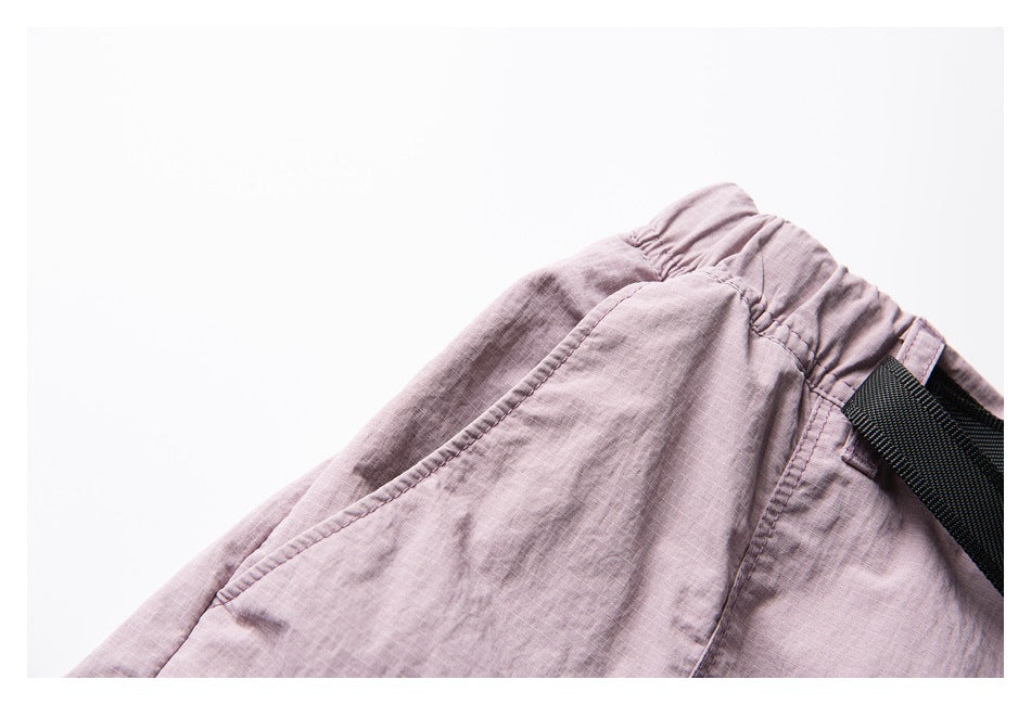 Close-up of dusty mauve shorts showing the gathered waistband, side seam and black webbing belt.