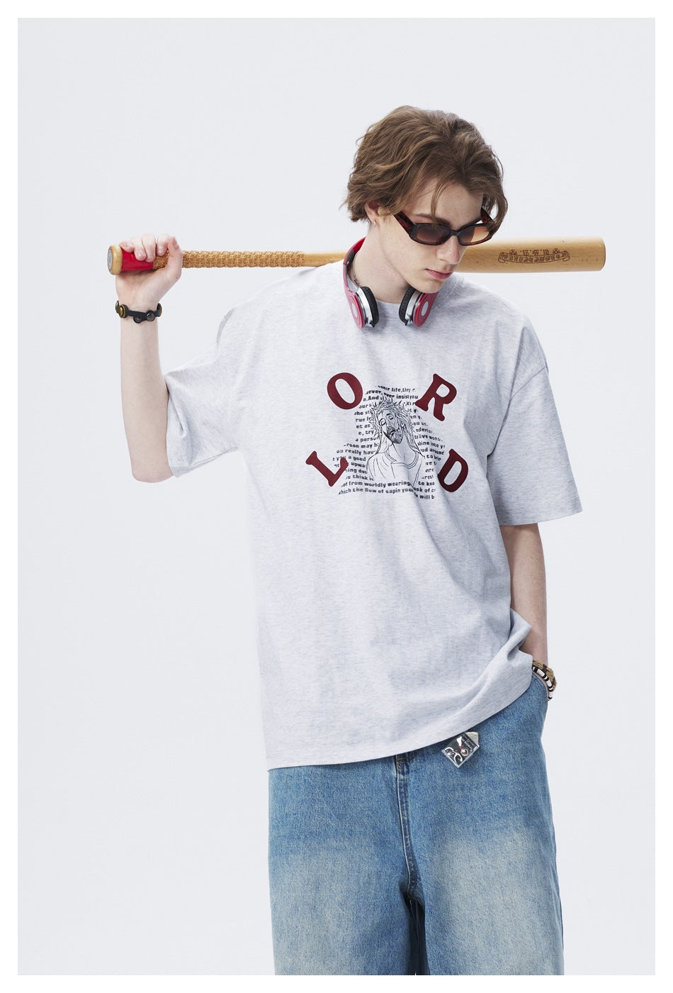 Model wearing a light gray oversized graphic T-shirt, shown with blue jeans and headphones.