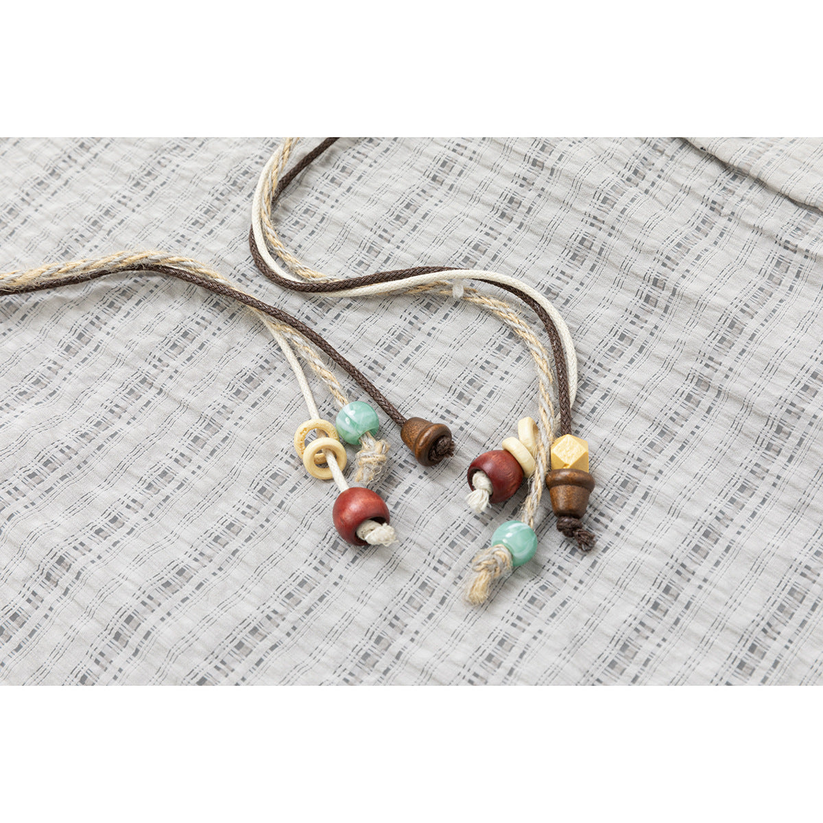 Close-up of braided jacket cords with colorful beads and wooden toggles against gray plaid fabric.