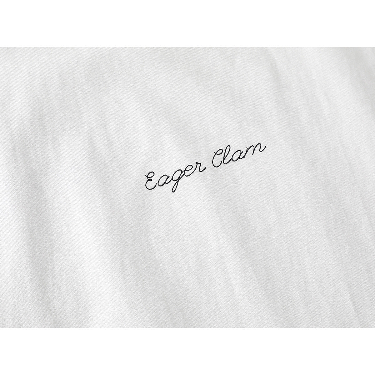 Close-up of black cursive “Eager Clan” lettering on white T-shirt fabric.