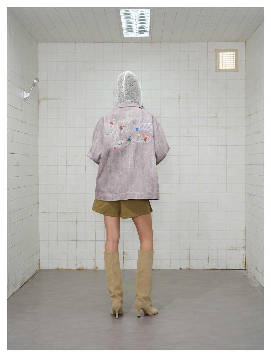 Back view of model wearing the mauve-pink jacket with large embroidered script lettering and flowers