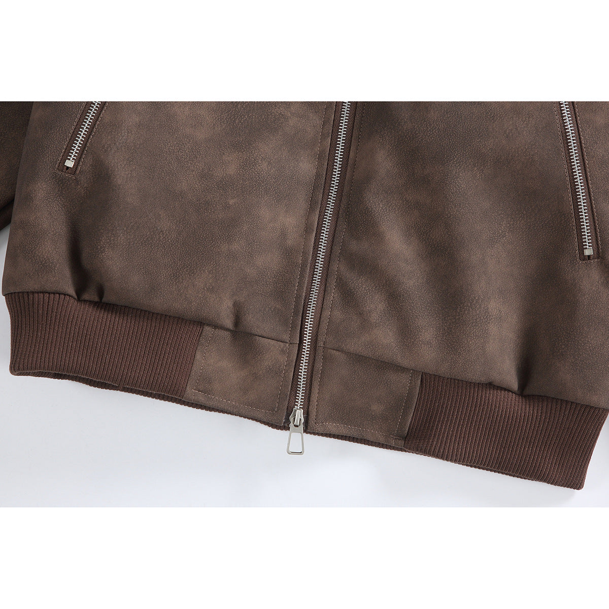 Close-up of the brown jacket’s lower front, showing the center zipper, angled pocket zippers and ribbed hem.