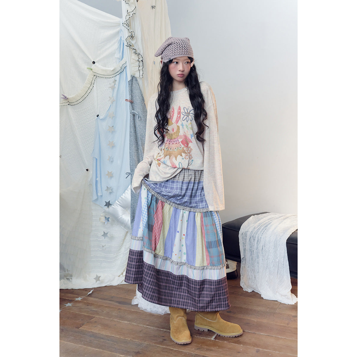 Model lifts her blue and multicolor tiered patchwork skirt, showing its layered plaid, check and polka-dot panels.