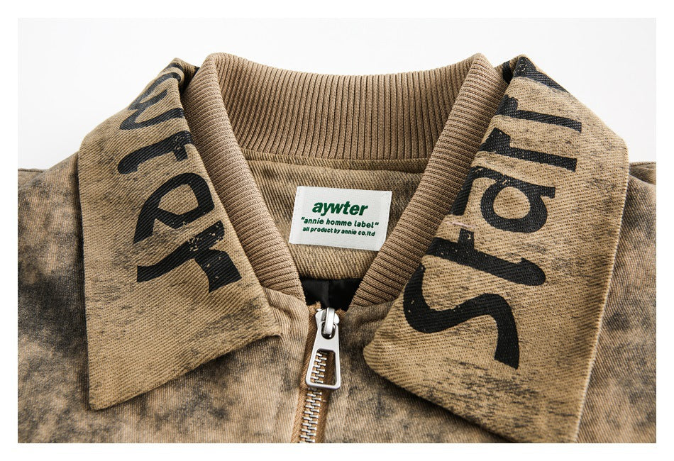 Close-up of a tan mottled jacket collar with oversized black lettering, front zipper, and sewn neck label.
