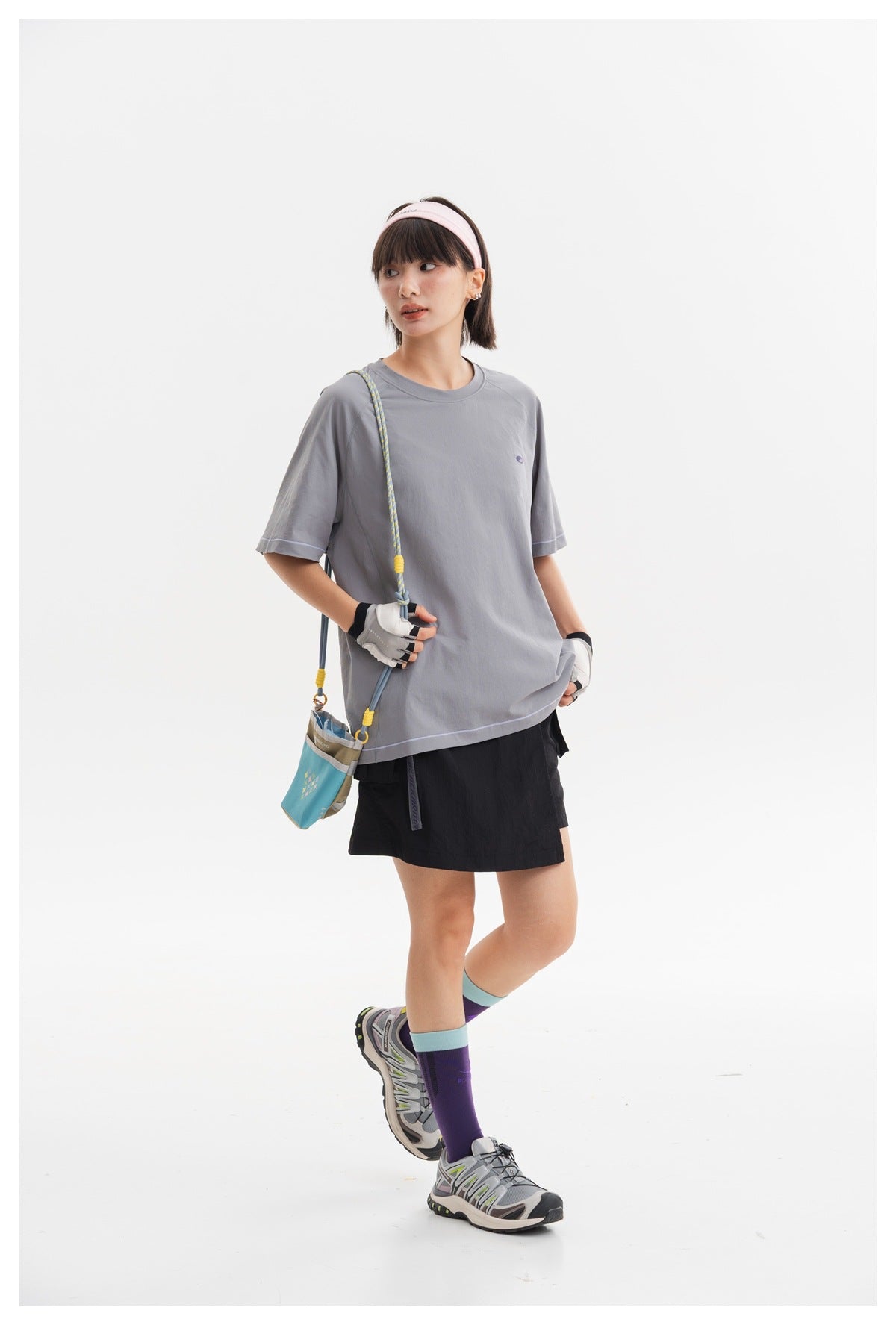 Three-quarter view of a model wearing an oversized gray T-shirt and black shorts with a crossbody pouch.