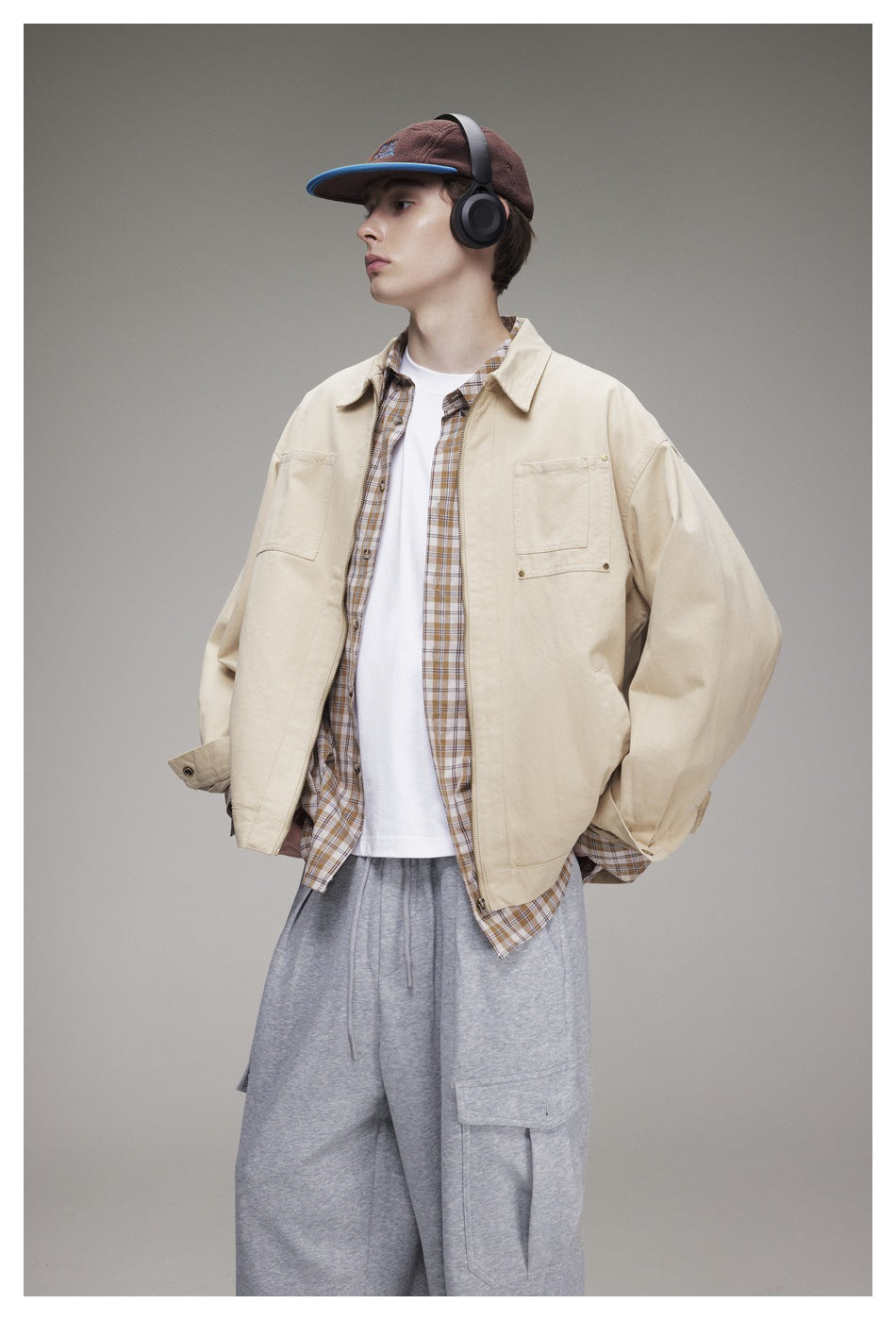 Closer view of a model wearing a light beige utility jacket over a plaid shirt and white tee, with gray cargo pants.