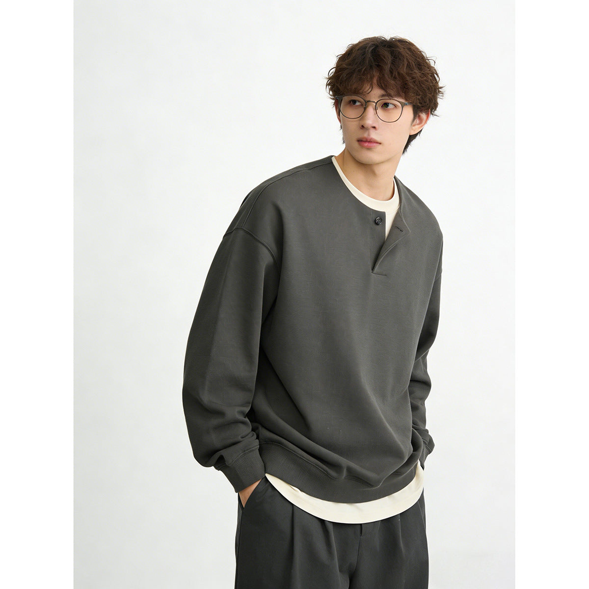 Model wearing a charcoal oversized sweatshirt with a short button placket and cream layer underneath.