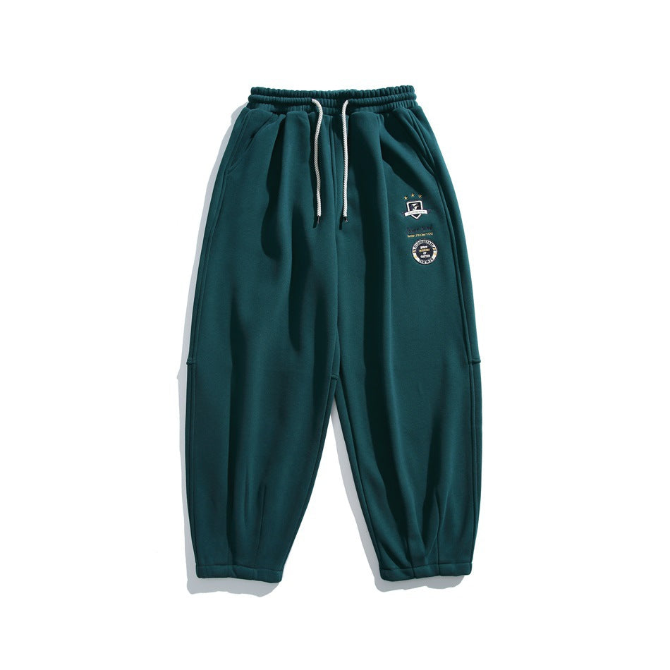 Dark green sweatpants flat lay with drawstring waist, side pockets and embroidered badges on the left leg