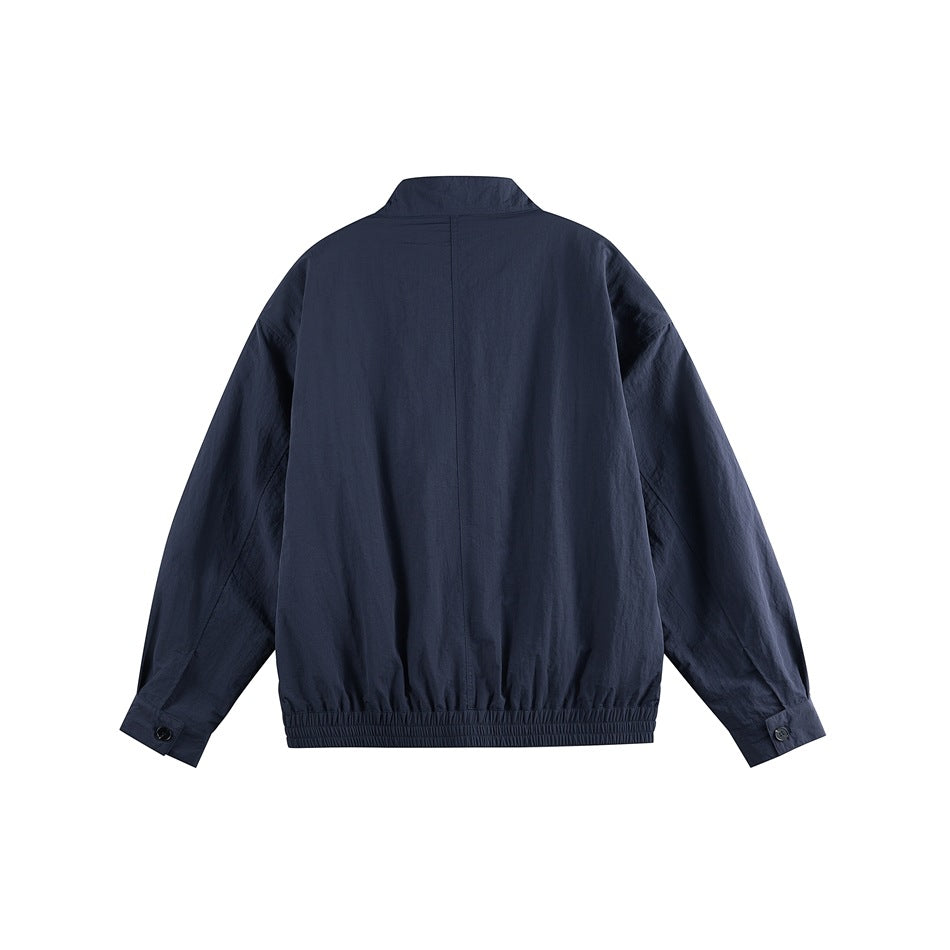 Back view of a dark navy jacket laid flat, with long sleeves, a short stand collar, button cuffs and gathered hem.