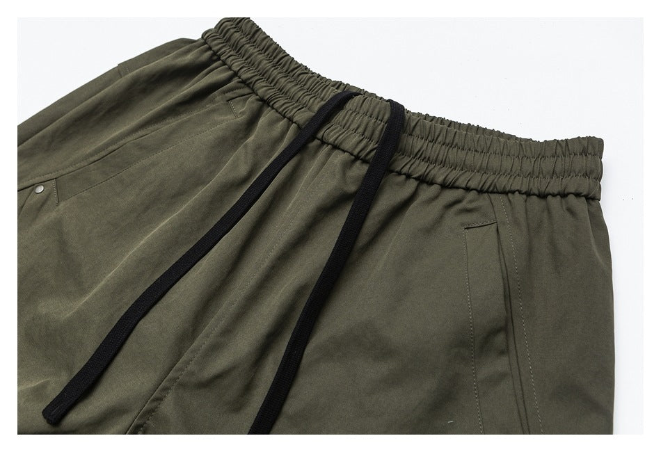 Close-up of olive trousers showing the elastic waist, black drawstrings, and pocket details.