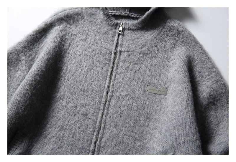 Close-up of a gray fuzzy zip-up cardigan showing its stand collar, front zipper and small metal chest badge.