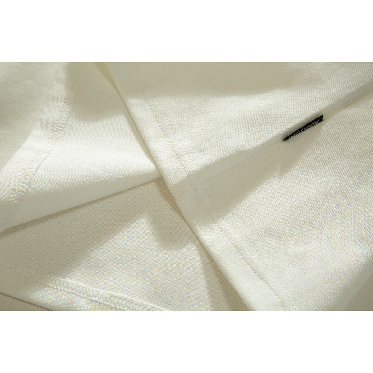 Close-up of an off-white T-shirt's seams and hem with a small black side tag.