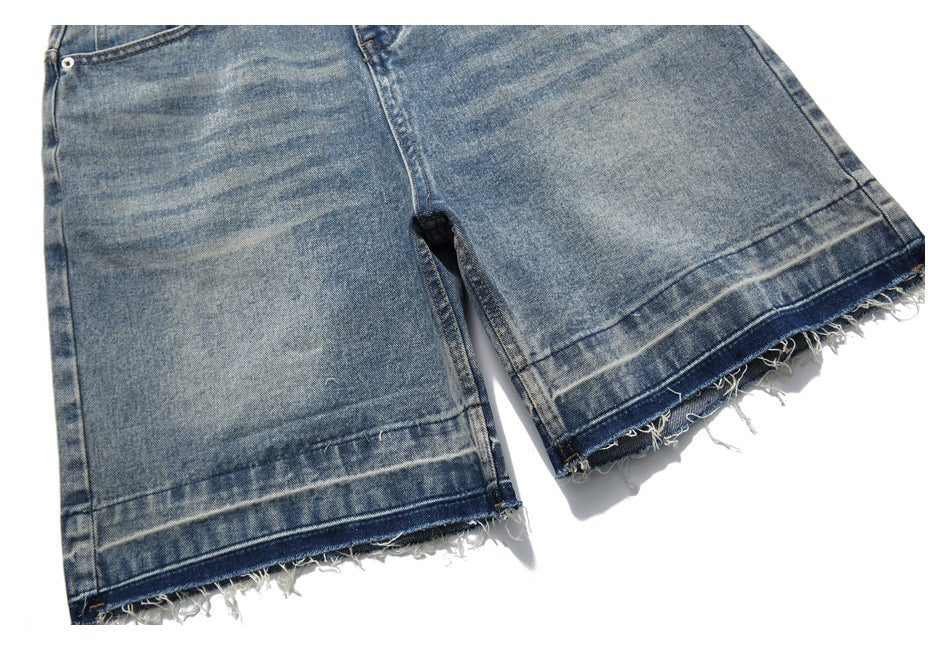 Close-up of blue washed denim legs with wide raw hems and frayed edges.