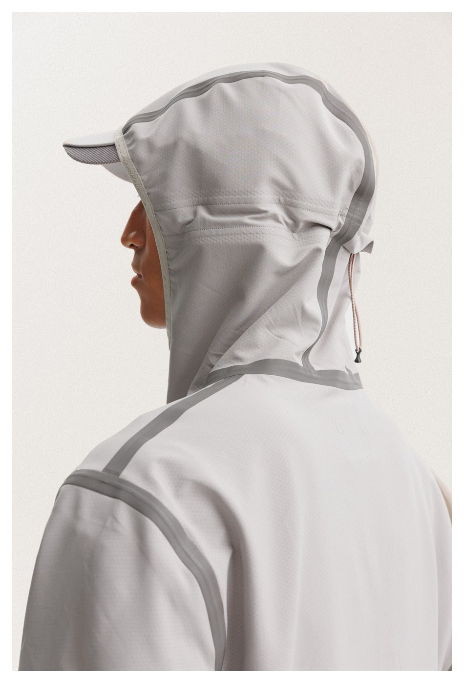 Close-up of a model wearing the light gray jacket, showing its hood, cap brim, drawcord, and shoulder seams.