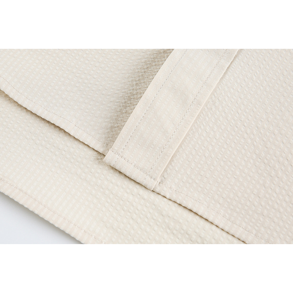 Close-up of the cream garment’s stitched hem and overlapping fabric panels.