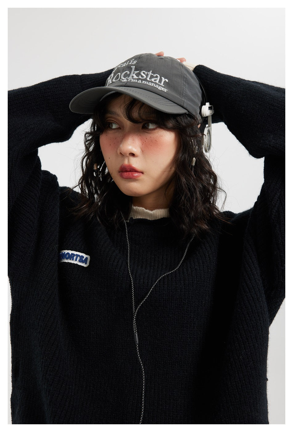 Close view of a model wearing a black ribbed sweater with cream collar and a small chest patch.