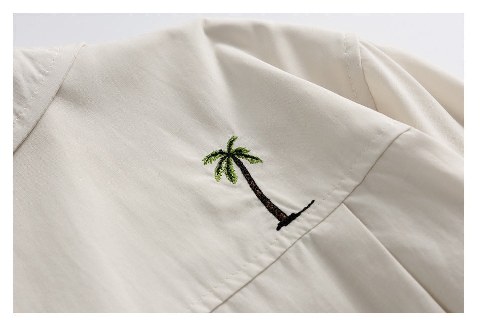 Close-up of a small embroidered palm tree on pale beige fabric.