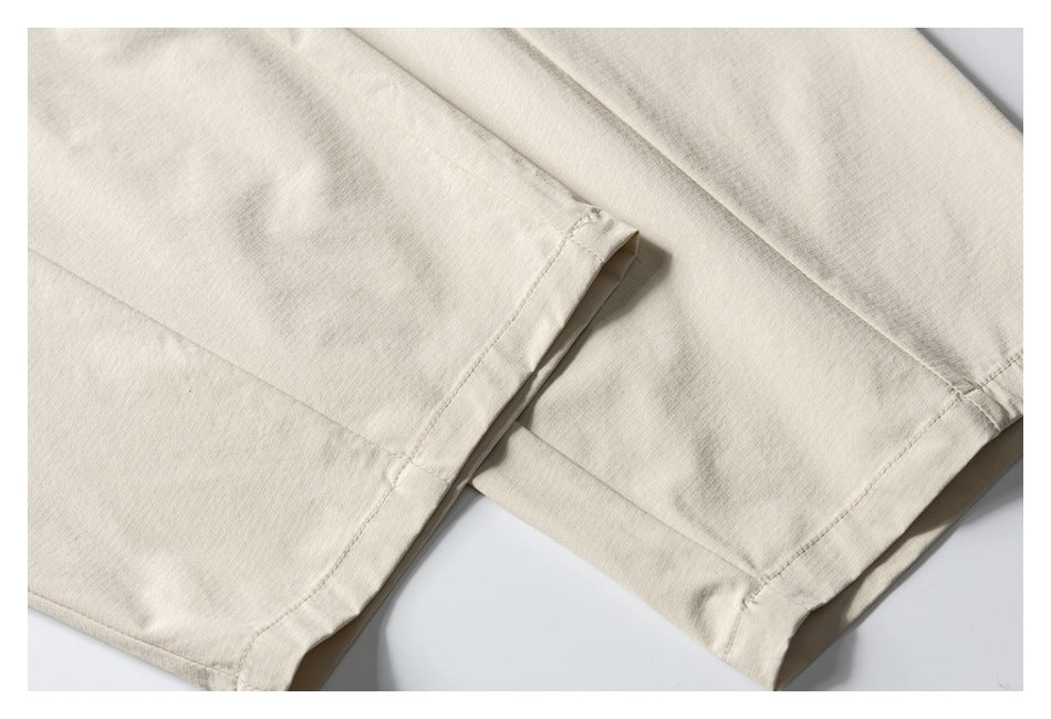 Close-up of the stitched hems and overlapping legs of light beige trousers.