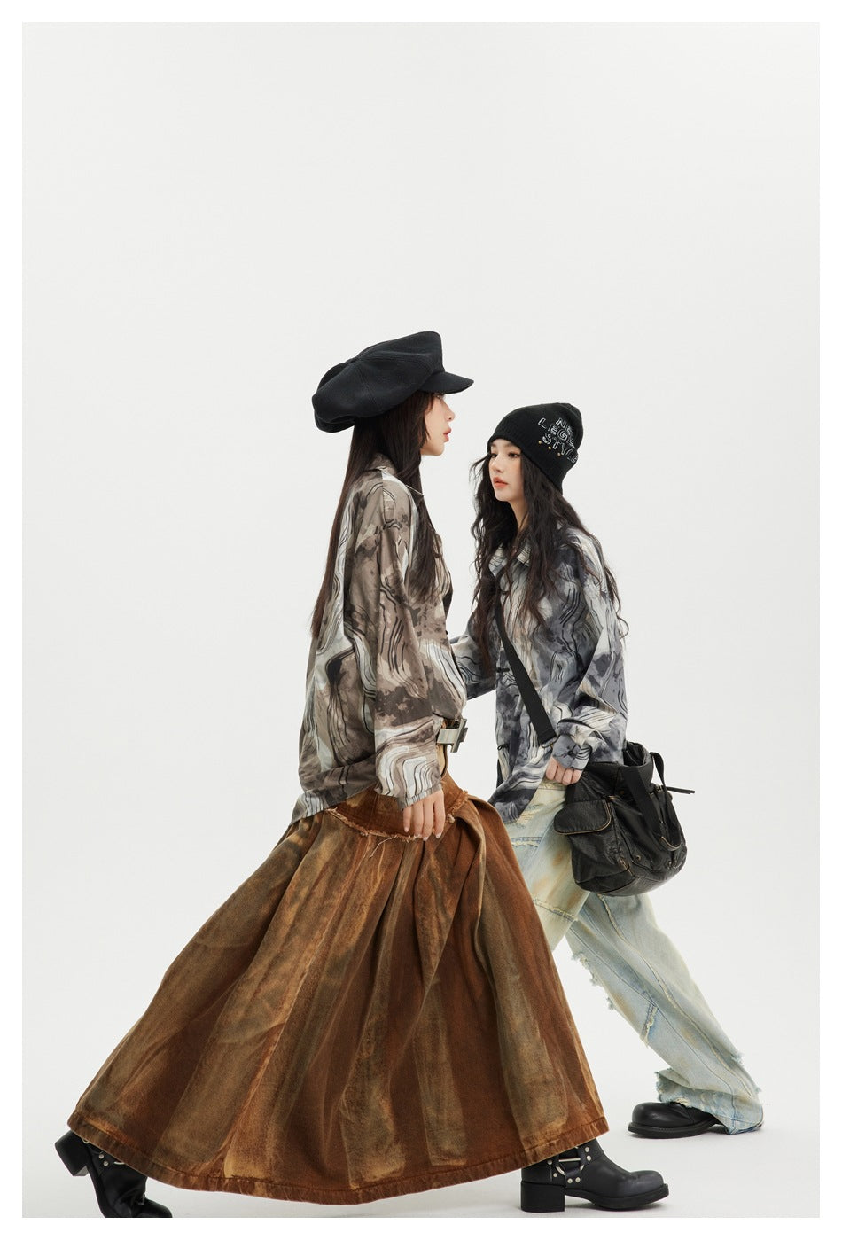 Two models in profile wear loose brown- and gray-toned abstract-pattern shirts with a long skirt and distressed jeans.