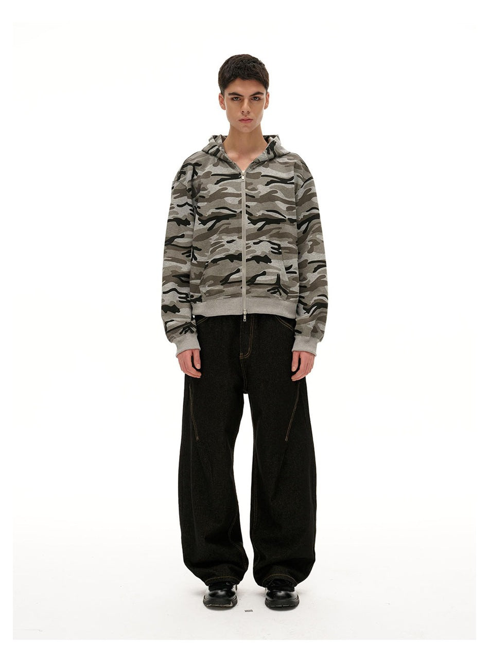Front view of a model wearing a gray camouflage zip-up hoodie with the hood down and loose black jeans.