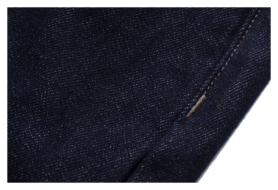 Close-up of dark indigo denim with a diagonal seam and a small area of frayed tan stitching.