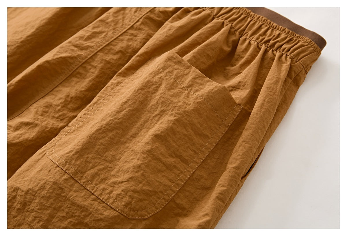Close-up of a large stitched patch pocket on camel-brown shorts, with the gathered waistband visible above.