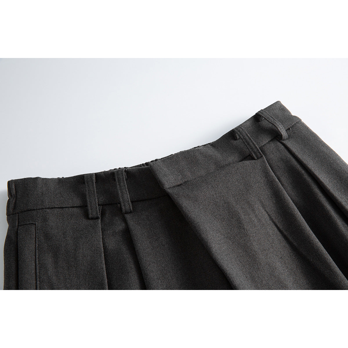 Close-up of dark charcoal trousers showing the waistband, belt loops, and front pleats.