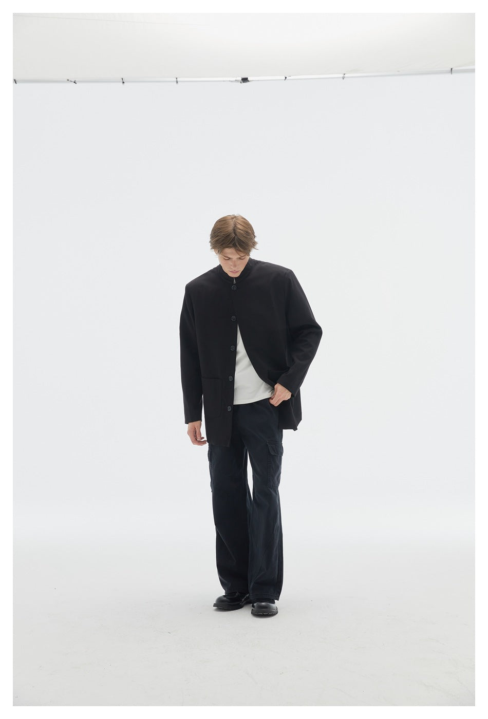 Model wearing a buttoned black stand-collar jacket with a patch pocket, white shirt and wide black cargo pants.