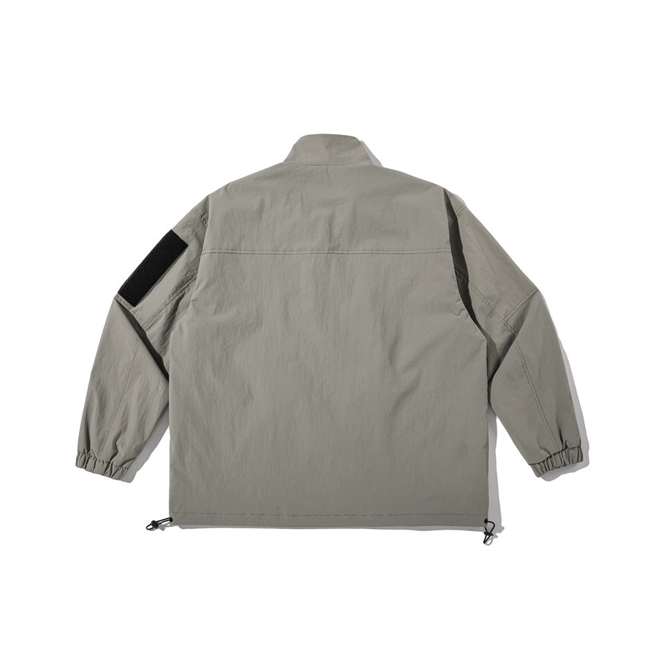 Back view of a gray jacket with a high collar, elastic cuffs, black sleeve patch and adjustable hem cords.