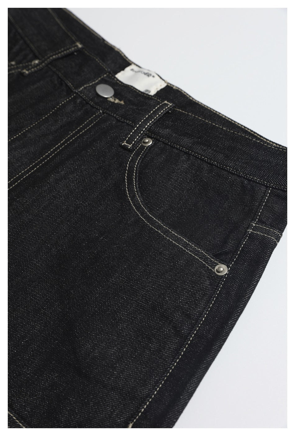 Detail of black jeans showing the waistband button, belt loop, front pocket and metal rivets.