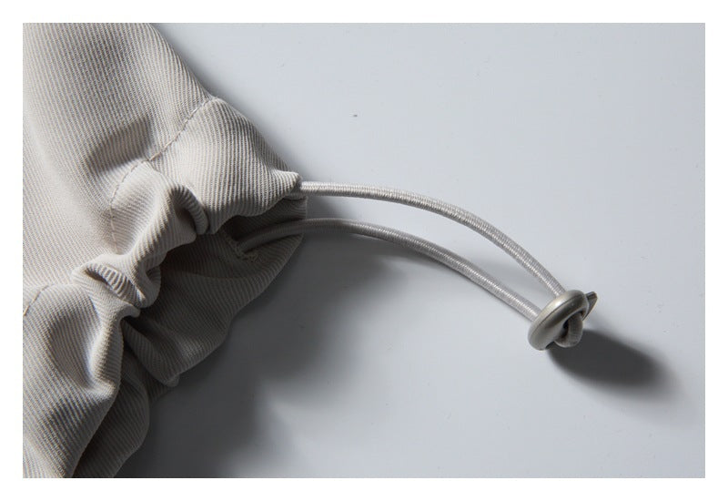 Close-up of a cord and round stopper emerging from the gathered cuff of the light gray pants.