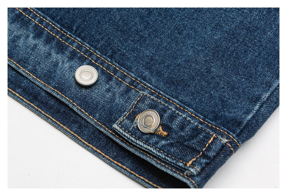 Close-up of dark blue denim with tan stitching and two silver metal snap fasteners.