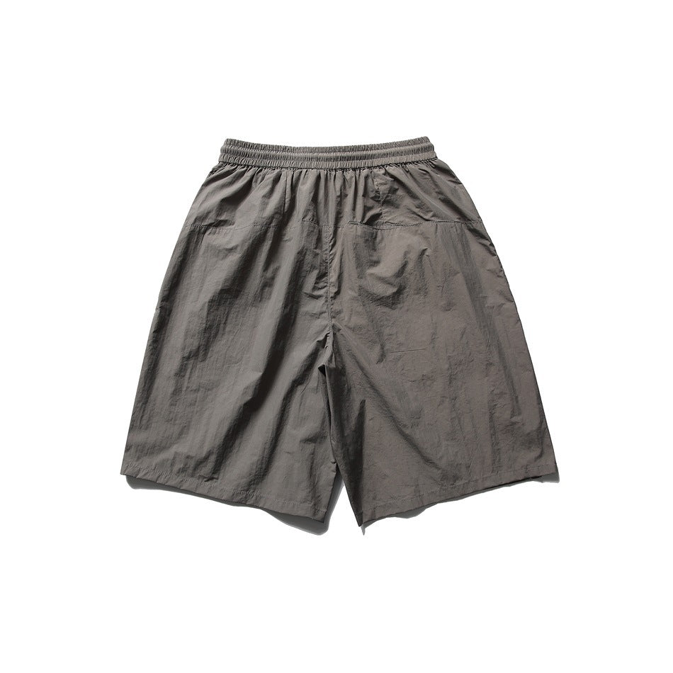Back view of loose charcoal-gray shorts with an elastic waistband and subtle welt pockets.