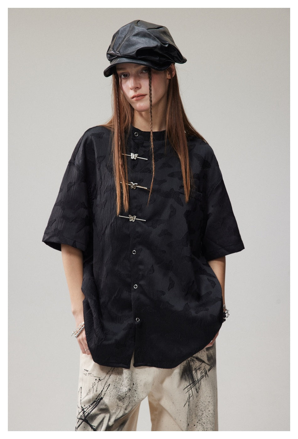 Close-up of a model in the black short-sleeve shirt showing butterfly toggle closures, snap buttons and a loose fit