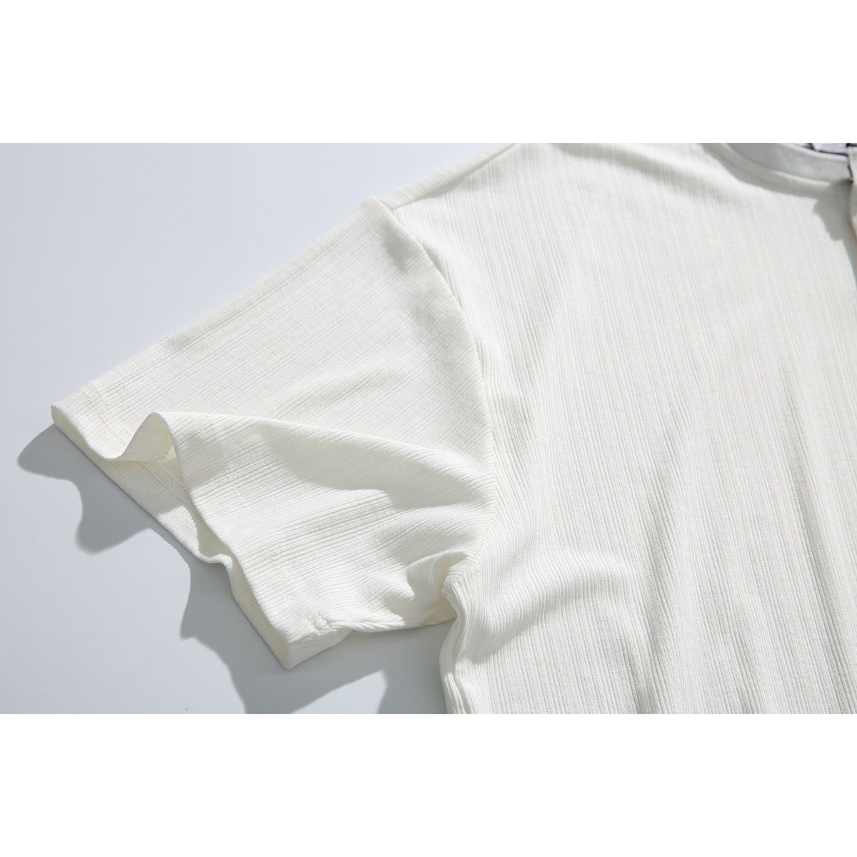 Close-up of the off-white shirt’s short sleeve, showing its ribbed texture and stitched cuff.