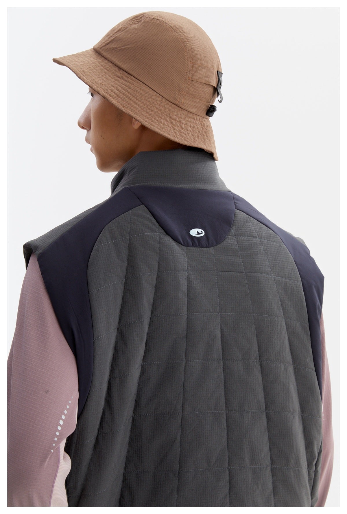 Rear view of a person wearing a charcoal quilted vest with dark navy panels and a tan bucket hat.