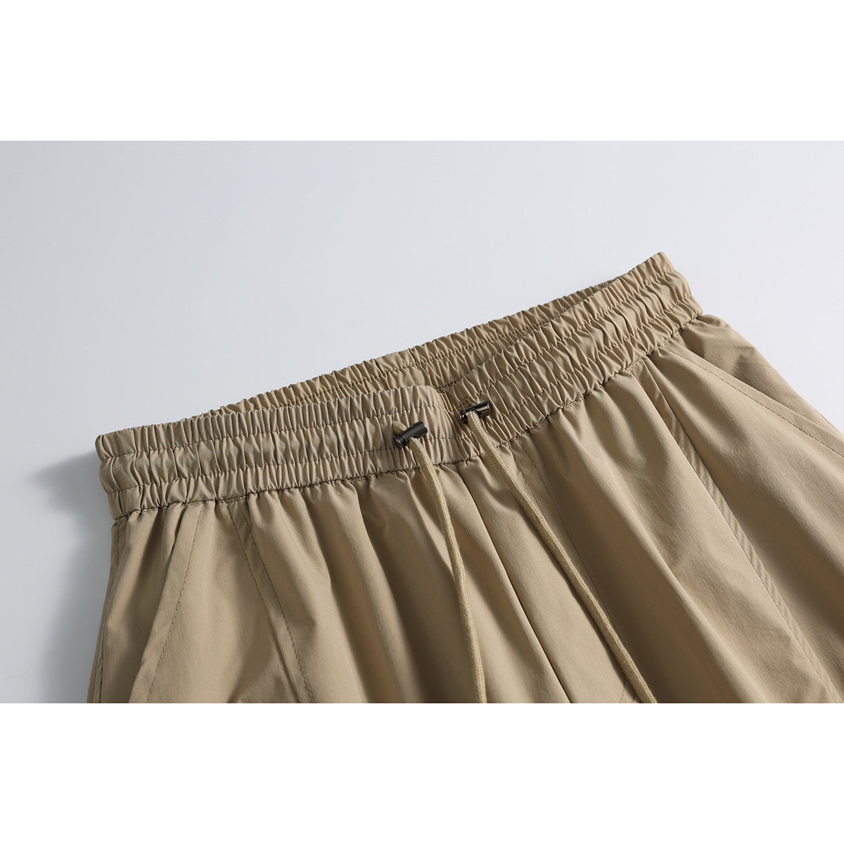 Close-up of tan wide-leg pants with a gathered elastic waistband, adjustable drawstrings, and angled seam details.