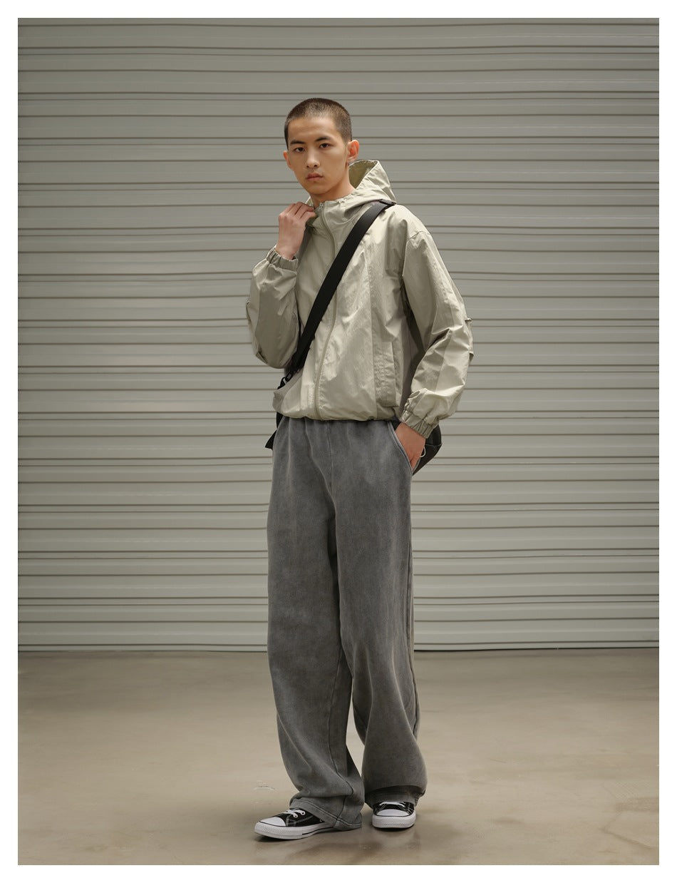 Model in a light beige hooded jacket and loose charcoal gray pants, posing at an angle with a black crossbody bag.