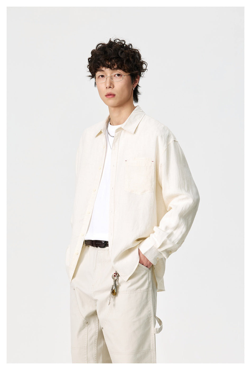 Model wearing an open ivory button-up shirt with a chest pocket over a white tee, paired with cream trousers.